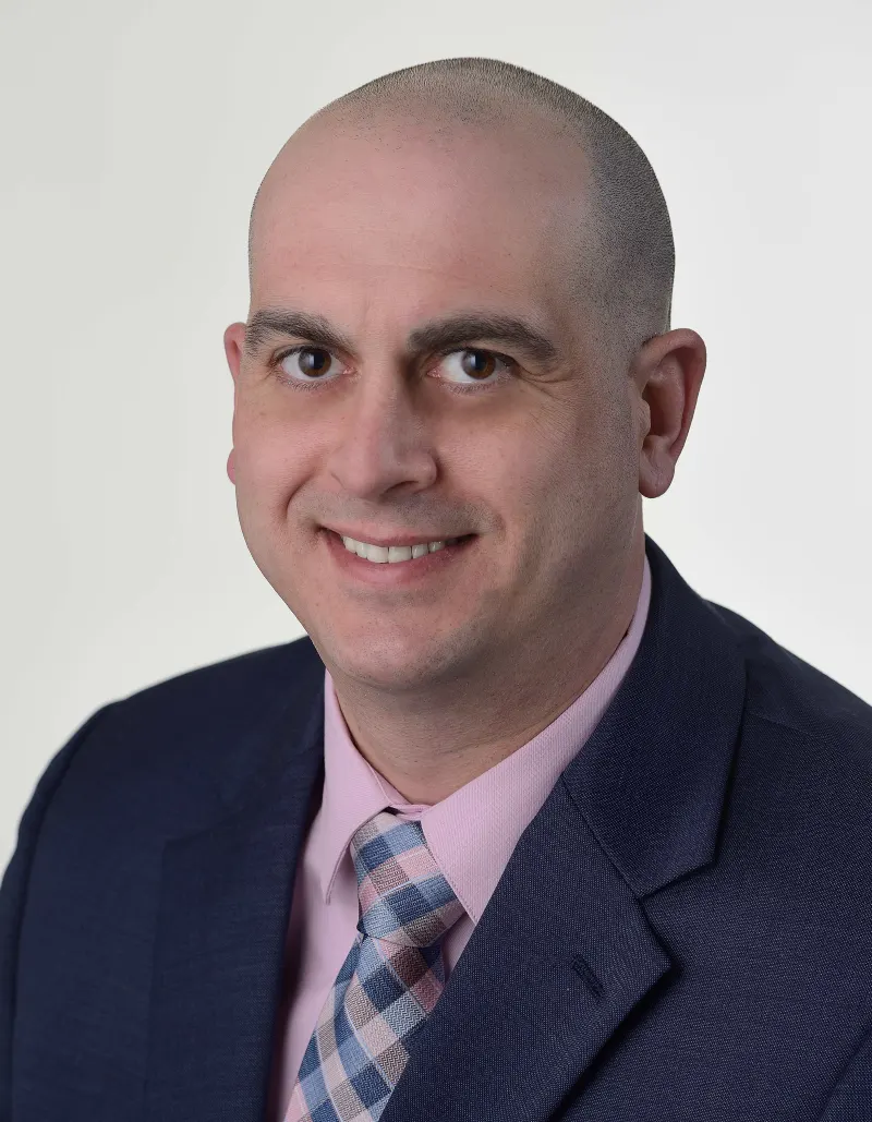Professional headshot of Bryan Loss in a navy suit and pink tie.